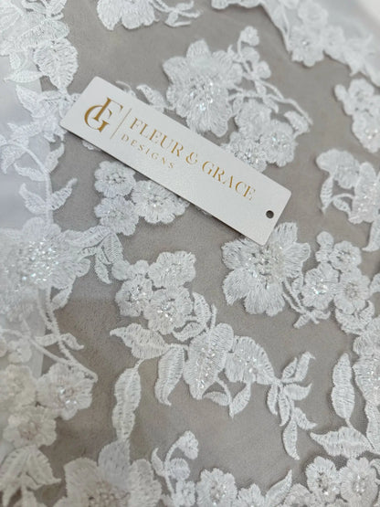 White floral lace appliqué with delicate beading on soft chiffon fabric, featuring a Fleur & Grace brand tag.
