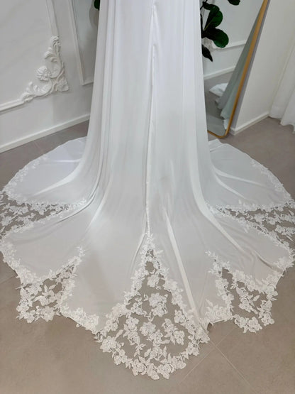 White chiffon wedding dress featuring a flowing A-line skirt and a chapel train with intricate floral lace appliqué.