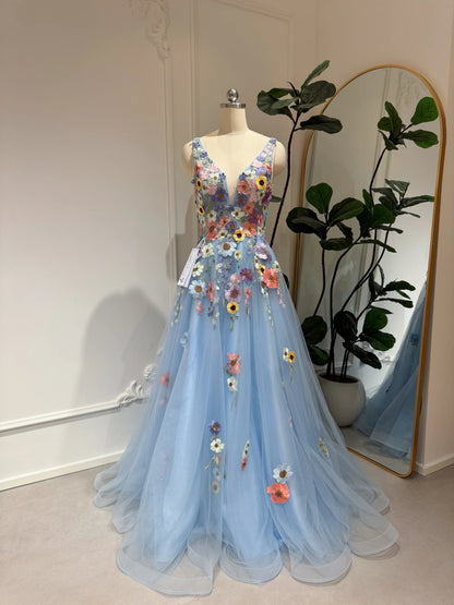 Blue floor-length gown with V-neck, sparkly mesh overlay, and colorful 3D wildflower embroidery on a dress form.