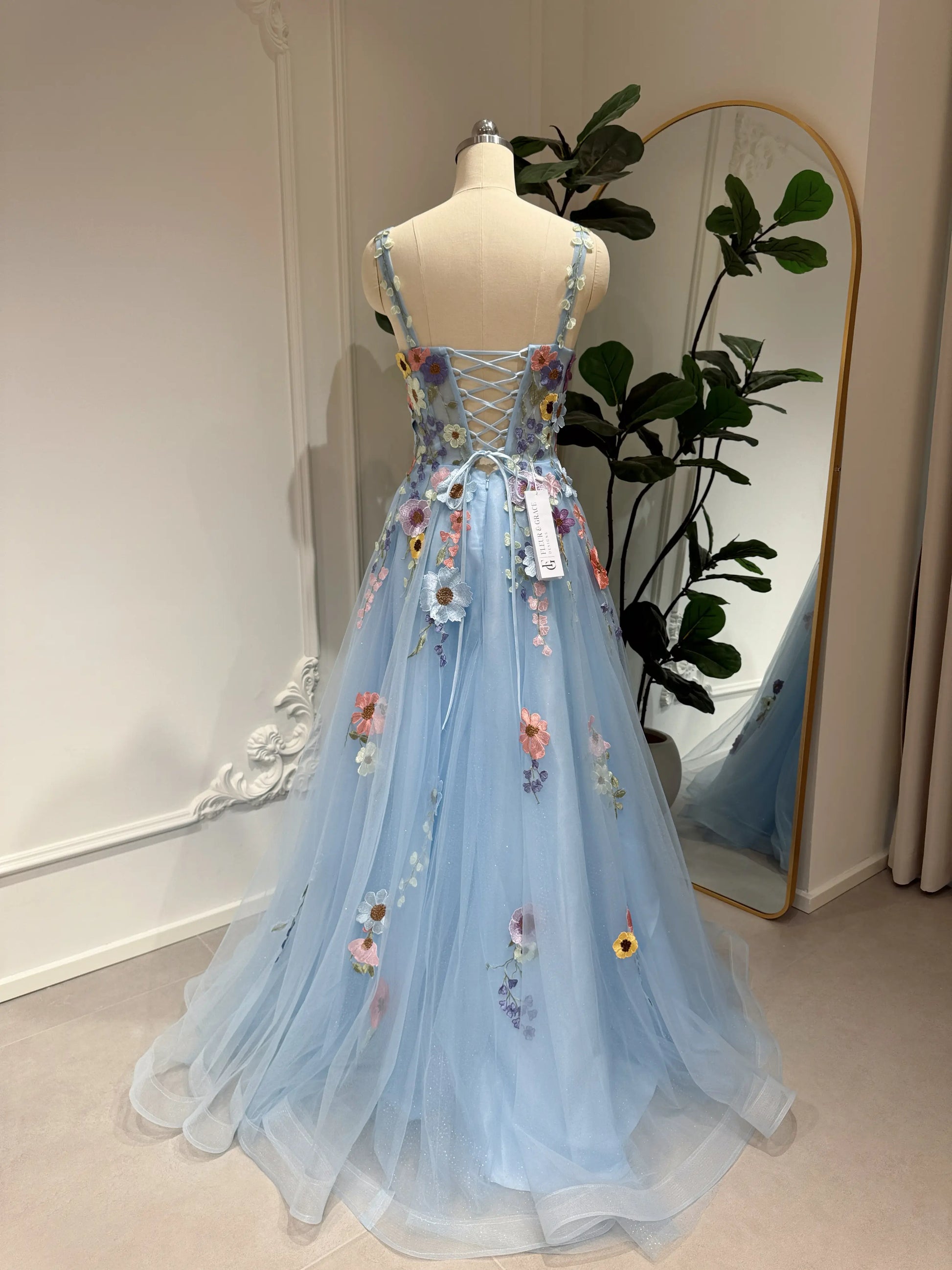 Blue floor-length gown with wildflower embroidery, sparkly mesh overlay, and a lace-up back on a dress form.