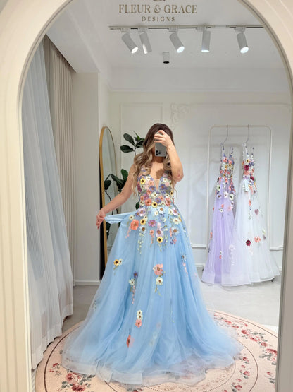 Blue floor-length gown with V-neck, sparkly mesh overlay, and colorful wildflower embroidery in a mirror reflection.