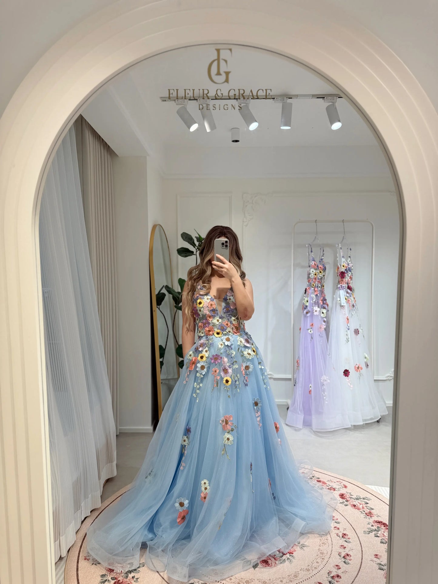 Blue floor-length gown with V-neck, sparkly mesh overlay, and colorful wildflower embroidery in a boutique mirror.