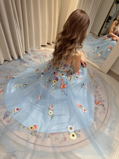 Blue floor-length gown with wildflower embroidery, sparkly mesh overlay, and a lace-up back, worn by a woman.