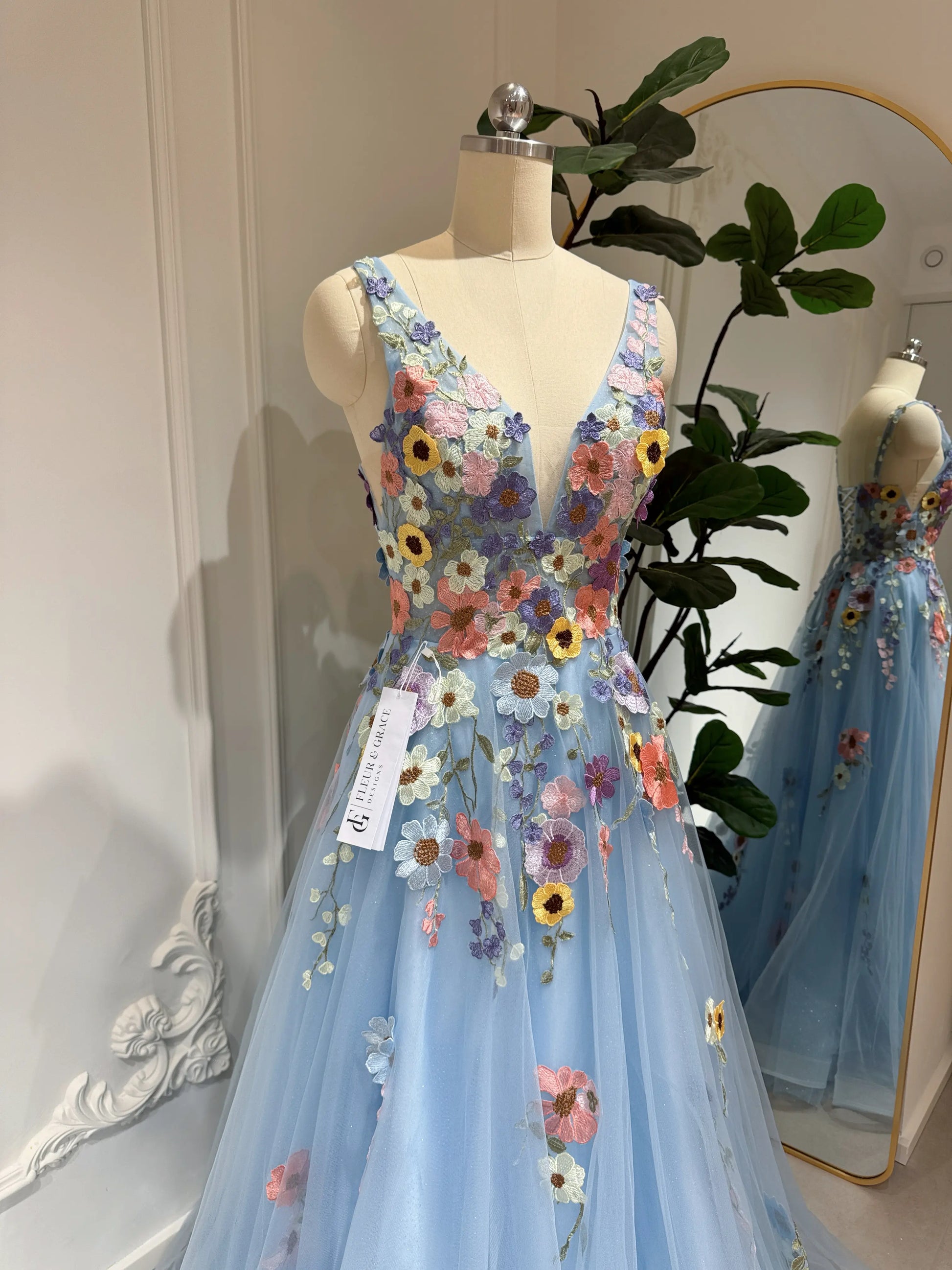 Blue floor-length gown with V-neckline, sparkly mesh, and colorful wildflower embroidery on a dress form.