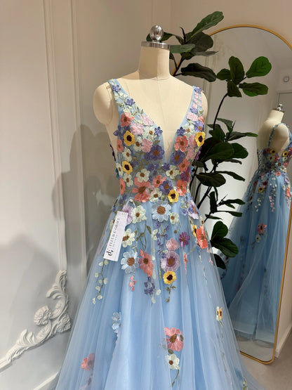 Blue floor-length gown with V-neckline, sparkly mesh, and colorful wildflower embroidery on a dress form.