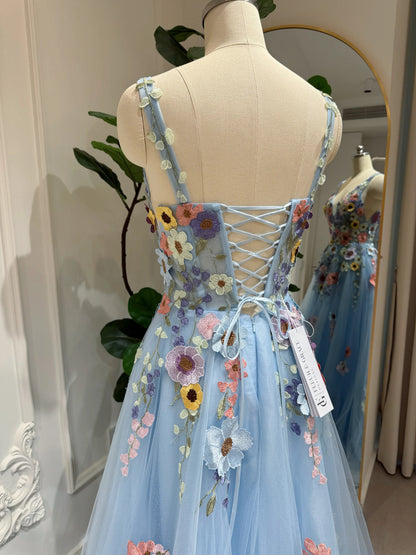 Blue floor-length gown with colorful wildflower embroidery, sparkly mesh overlay, and a lace-up corset back on a mannequin.