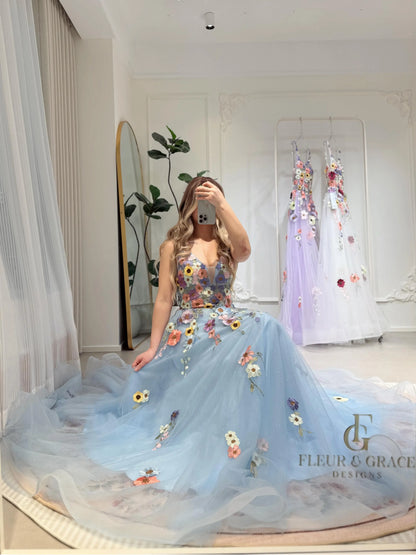 Blue floor-length gown with wildflower embroidery, V-neckline, and sparkly mesh overlay in a bright studio setting.