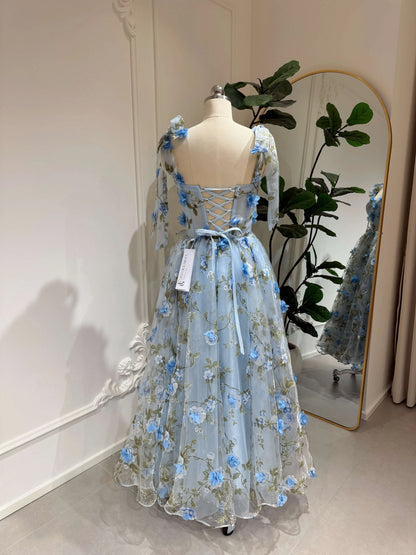Blue midi gown with 3D floral organza, green leaf prints, sweetheart neckline, and lace-up back on a mannequin.