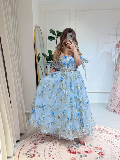 Blue ankle-length gown with 3D floral organza, green leaf prints, sweetheart neckline, and tie-shoulder straps.