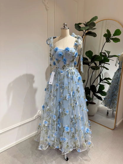 Blue midi gown with 3D floral organza, green leaf prints, sweetheart neckline, and tie-shoulder straps on a mannequin.