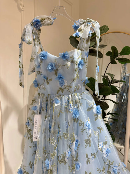 Blue ankle-length gown with 3D floral organza, green leaf prints, sweetheart neckline, and tie-shoulder straps.