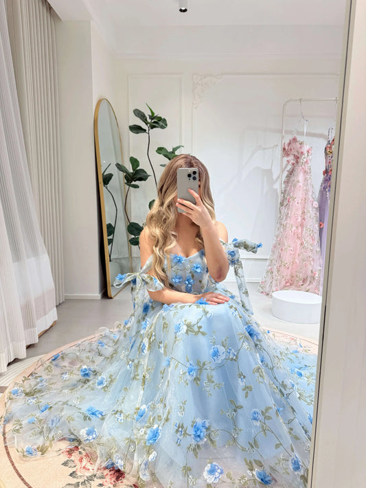 Blue ankle-length gown with 3D floral organza, green leaf prints, sweetheart neckline, and tie-strap sleeves.