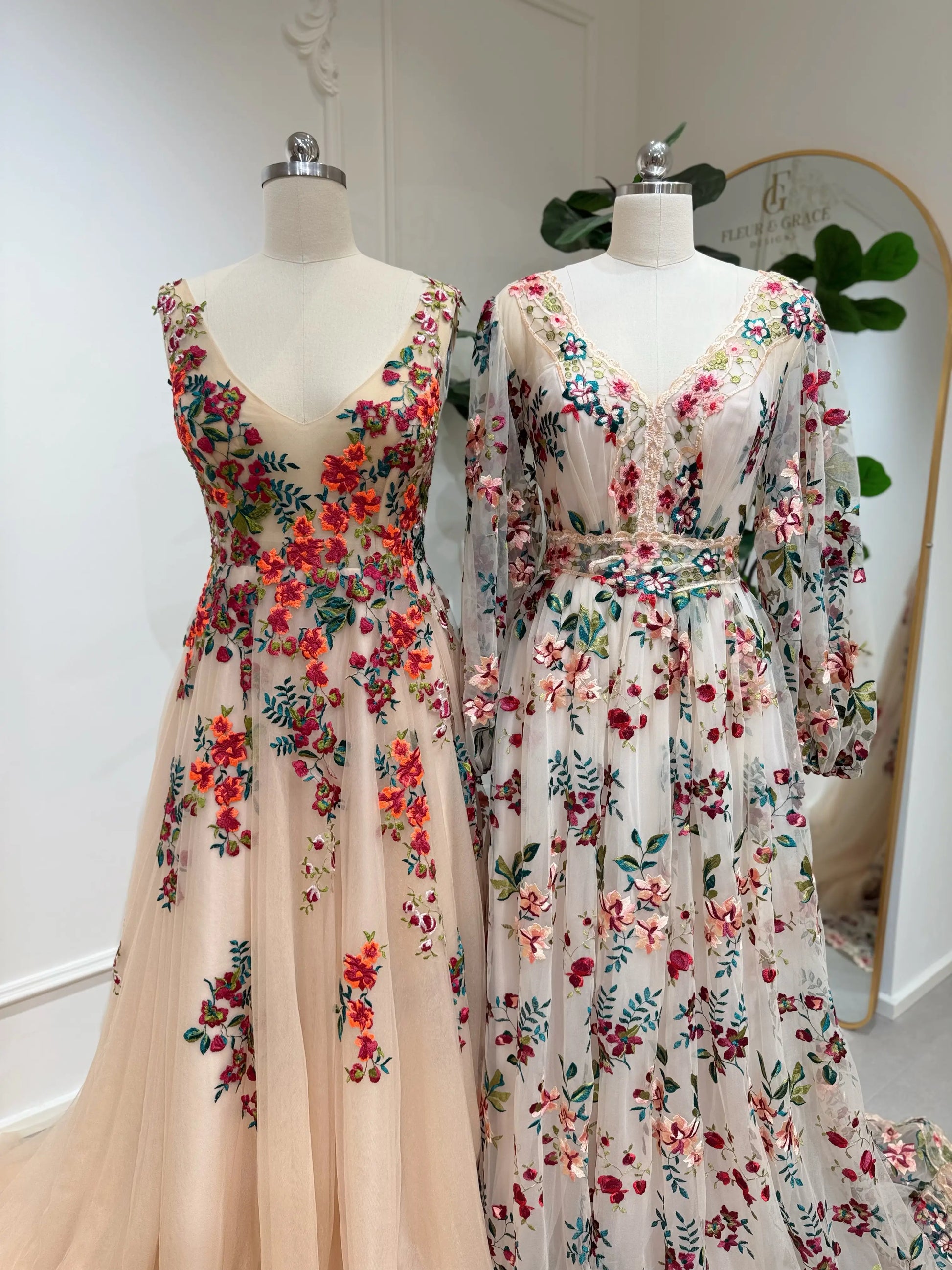 Bride mannequin wearing the Monica Gown by Fleur&Grace Designs — colorful wedding dress with orange floral appliqués, meadow green embroidery on champagne tulle, V-neck, sleeveless bodice, lace-up back, and pockets.