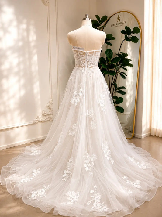 Strapless white A-line wedding dress with 3D floral lace appliqués on a layered tulle skirt and chapel train.