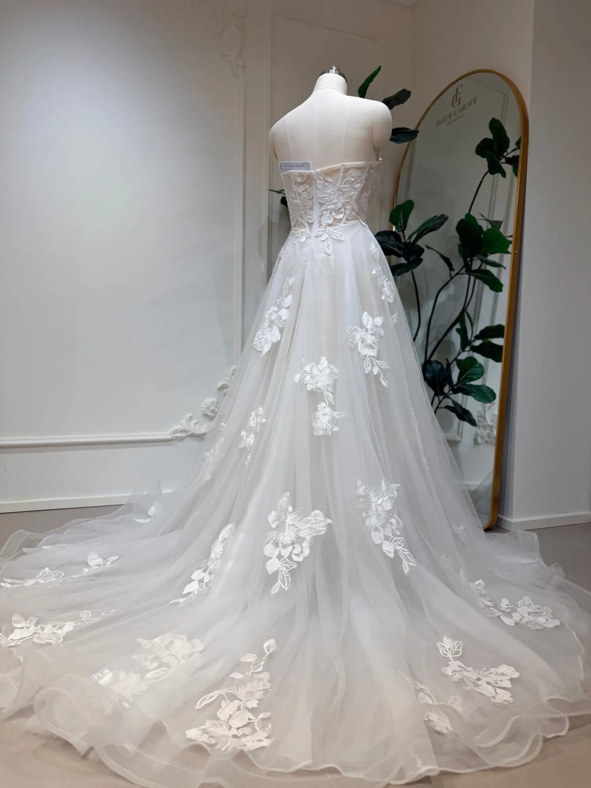 Strapless white A-line wedding dress with 3D floral lace appliqués and a flowing tulle chapel train on a mannequin.