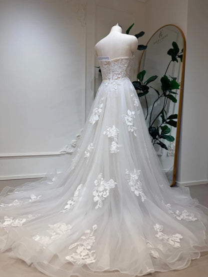 Strapless white A-line wedding dress with 3D floral lace appliqués and a flowing tulle chapel train on a mannequin.