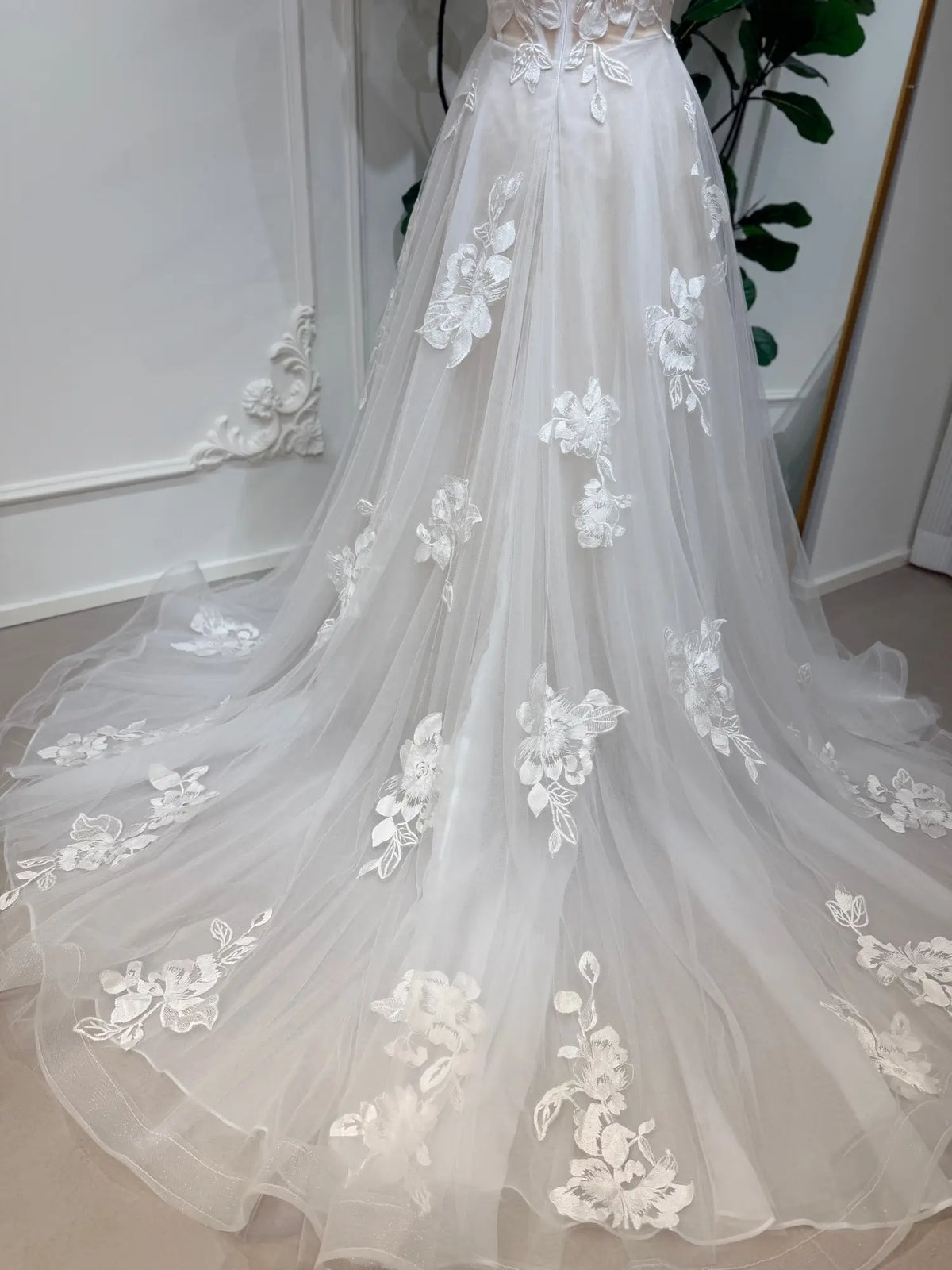 Strapless A-line wedding dress in white tulle with delicate 3D floral lace appliqués and a flowing chapel train.
