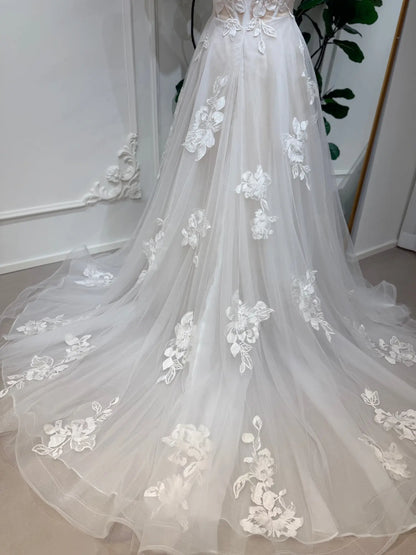 Strapless A-line wedding dress in white tulle with delicate 3D floral lace appliqués and a flowing chapel train.