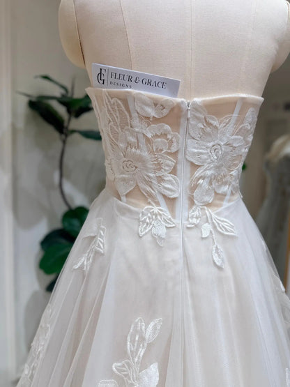 Strapless ivory wedding dress featuring a sheer bodice with intricate white 3D floral lace appliqués and tulle skirt.