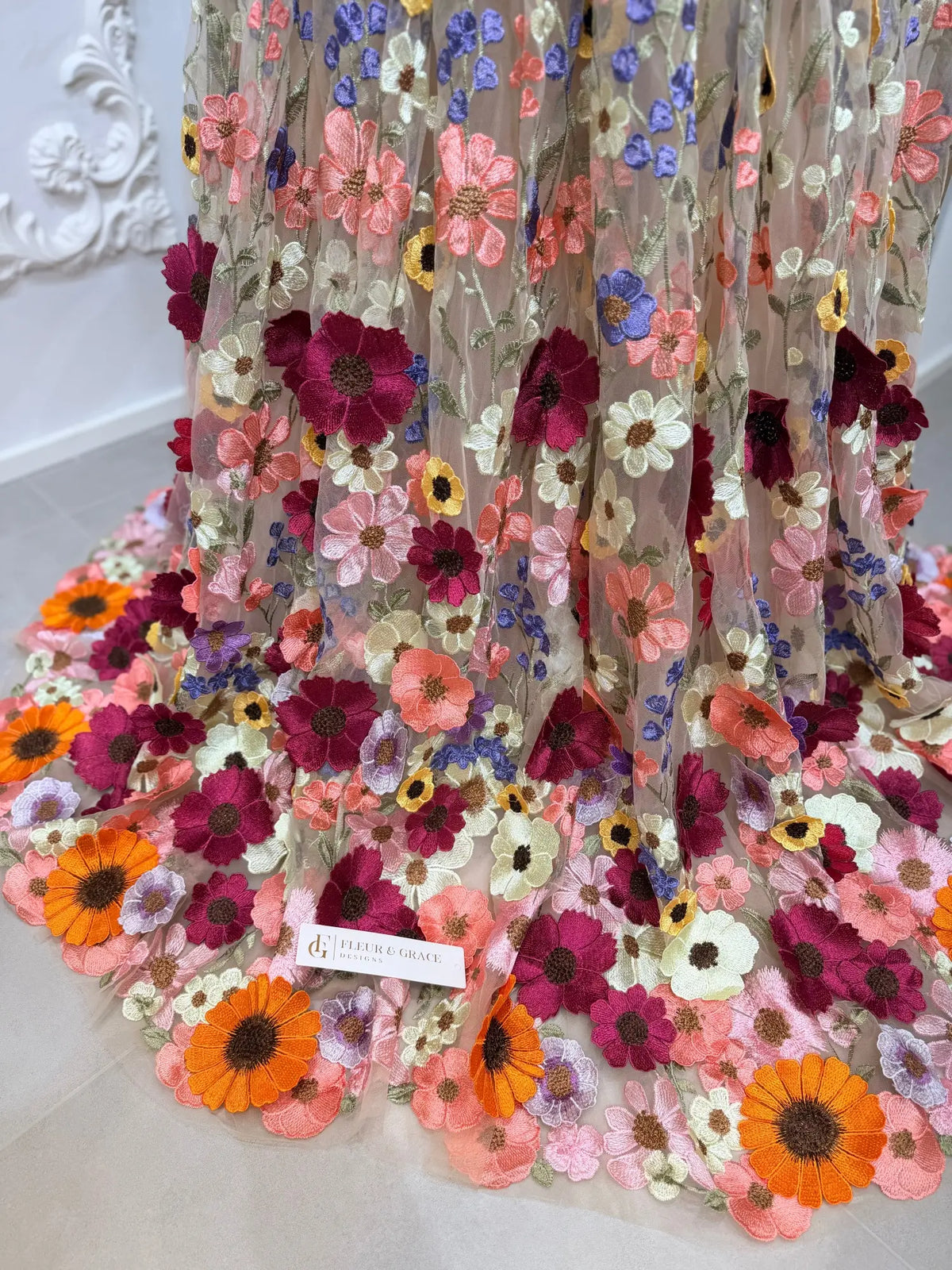 Close-up of sheer tulle wedding dress fabric featuring vibrant, multi-colored 3D floral embroidery in pink, orange, and purple.