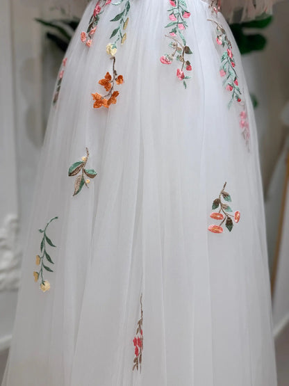 White tulle wedding dress featuring delicate hand-embroidered floral vines in pink, orange, and green accents.