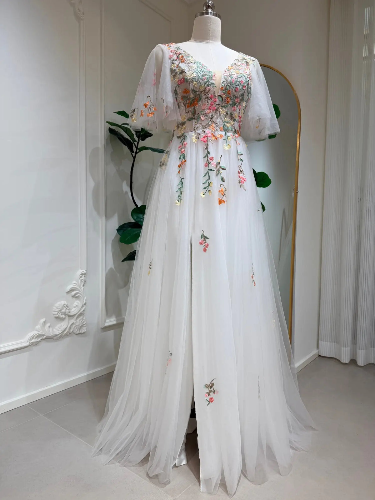 White A-line wedding dress with floral embroidery, flutter sleeves, V-neckline, and a side slit on a tulle skirt.