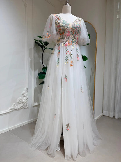 White A-line wedding dress with floral embroidery, flutter sleeves, V-neckline, and a side slit on a tulle skirt.