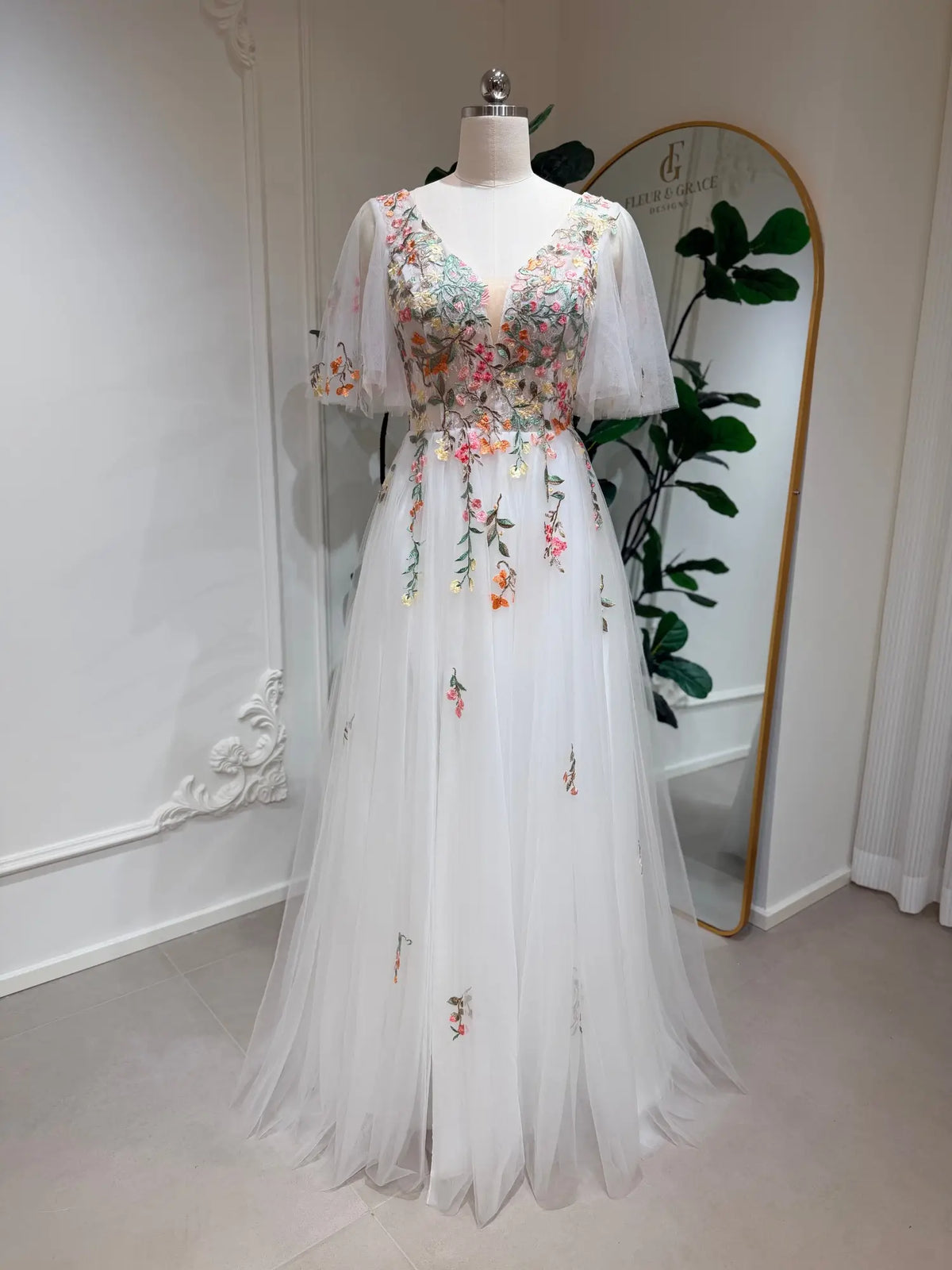 White A-line wedding dress with floral embroidery, V-neckline, and flutter sleeves on a mannequin.