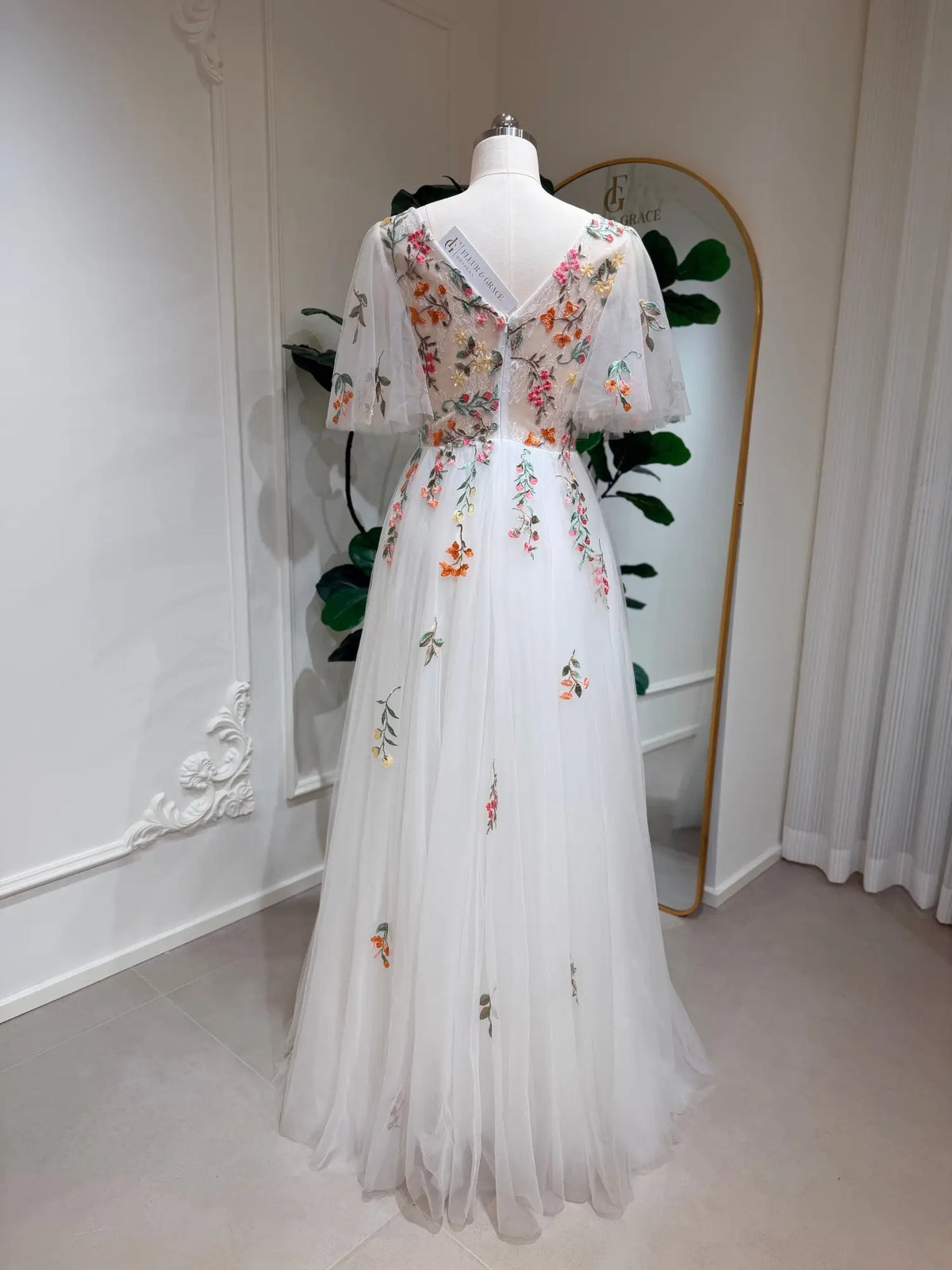 White A-line wedding dress with flutter sleeves, V-neck, and colorful floral embroidery on tulle fabric.
