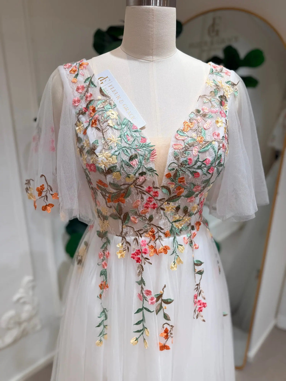 White tulle wedding dress with a V-neck, flutter sleeves, and colorful floral vine embroidery on the bodice.