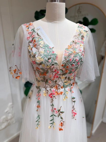 White tulle wedding dress with a V-neck, flutter sleeves, and colorful floral vine embroidery on the bodice.