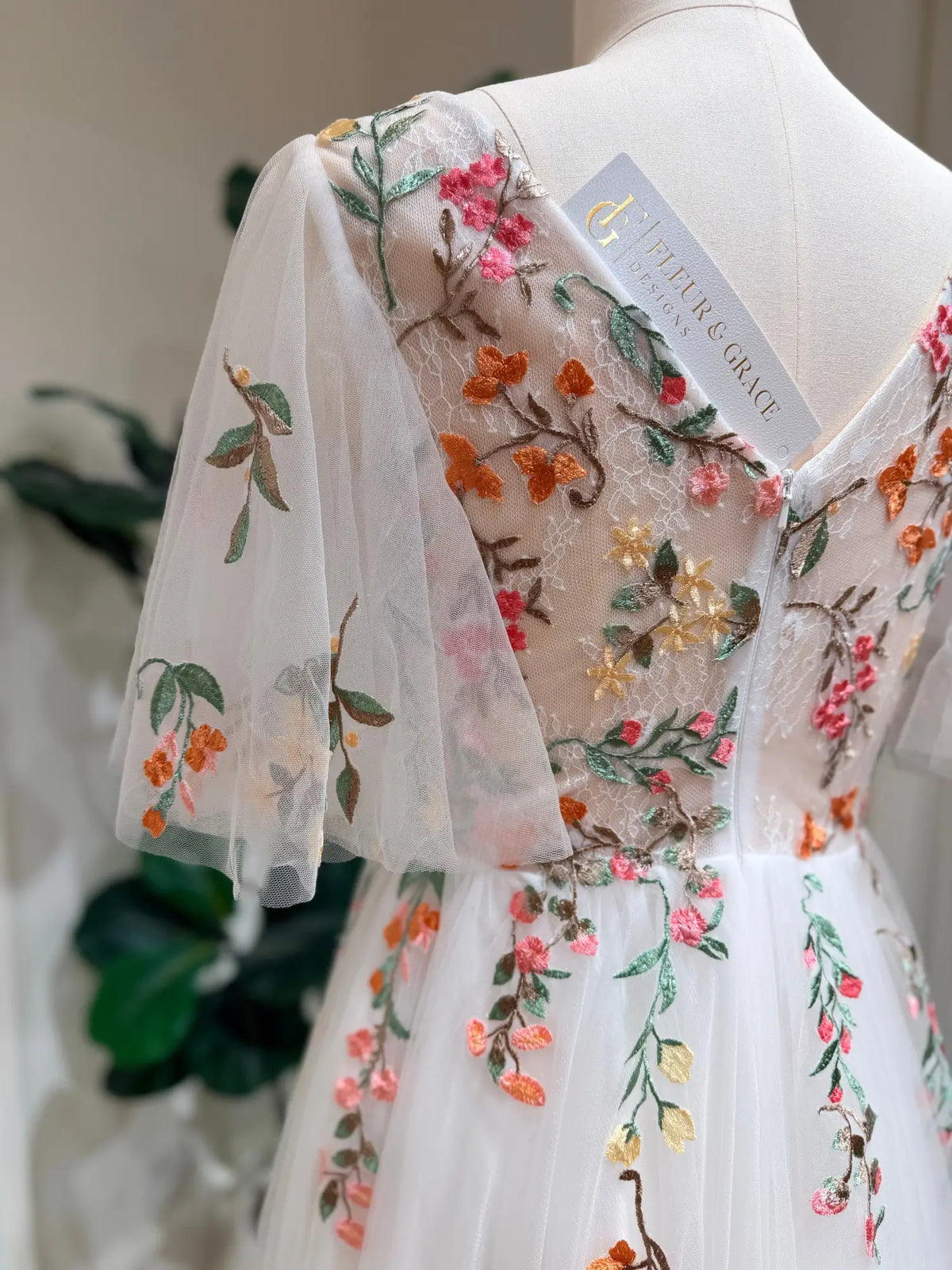White tulle wedding dress with colorful floral embroidery, V-neckline, and airy flutter sleeves on a mannequin.