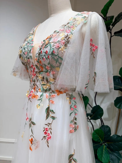 White tulle wedding dress with colorful floral embroidery, V-neckline, and airy flutter sleeves on a mannequin.
