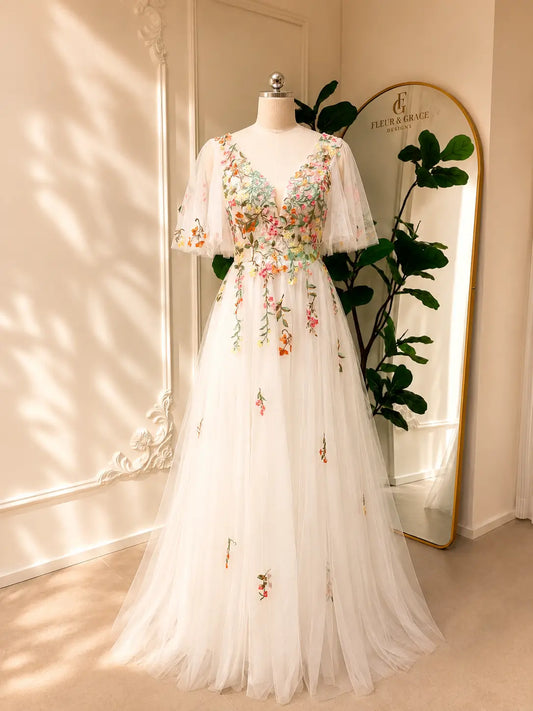 White A-line wedding dress with colorful floral embroidery, V-neckline, and airy flutter sleeves on a mannequin.