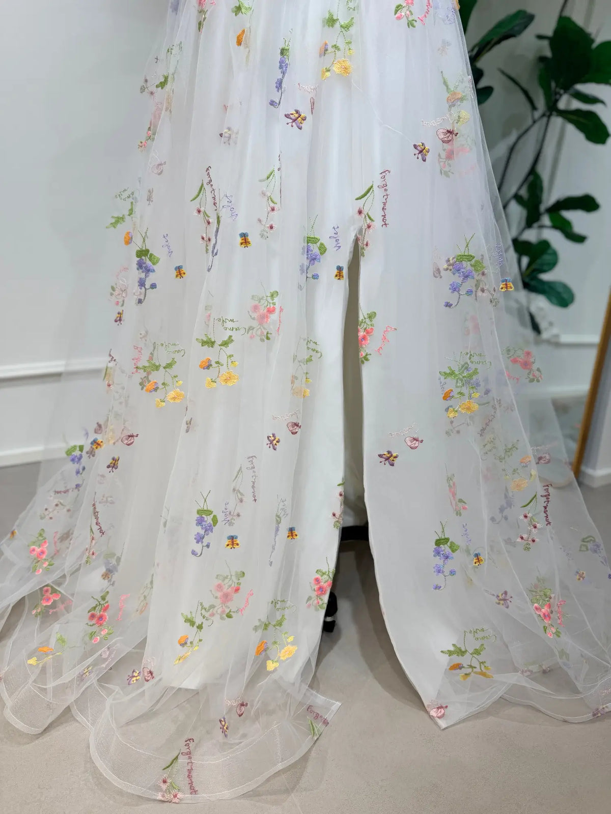 White A-line wedding dress featuring colorful pastel floral embroidery on layered tulle with a front leg slit.