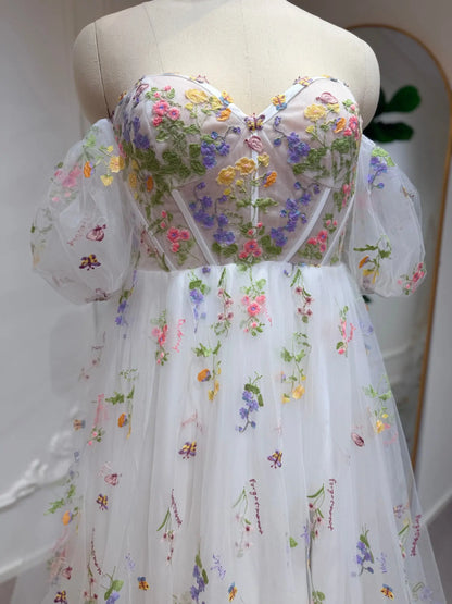 White A-line wedding dress with pastel floral embroidery, corset bodice, and detachable sheer puff sleeves.