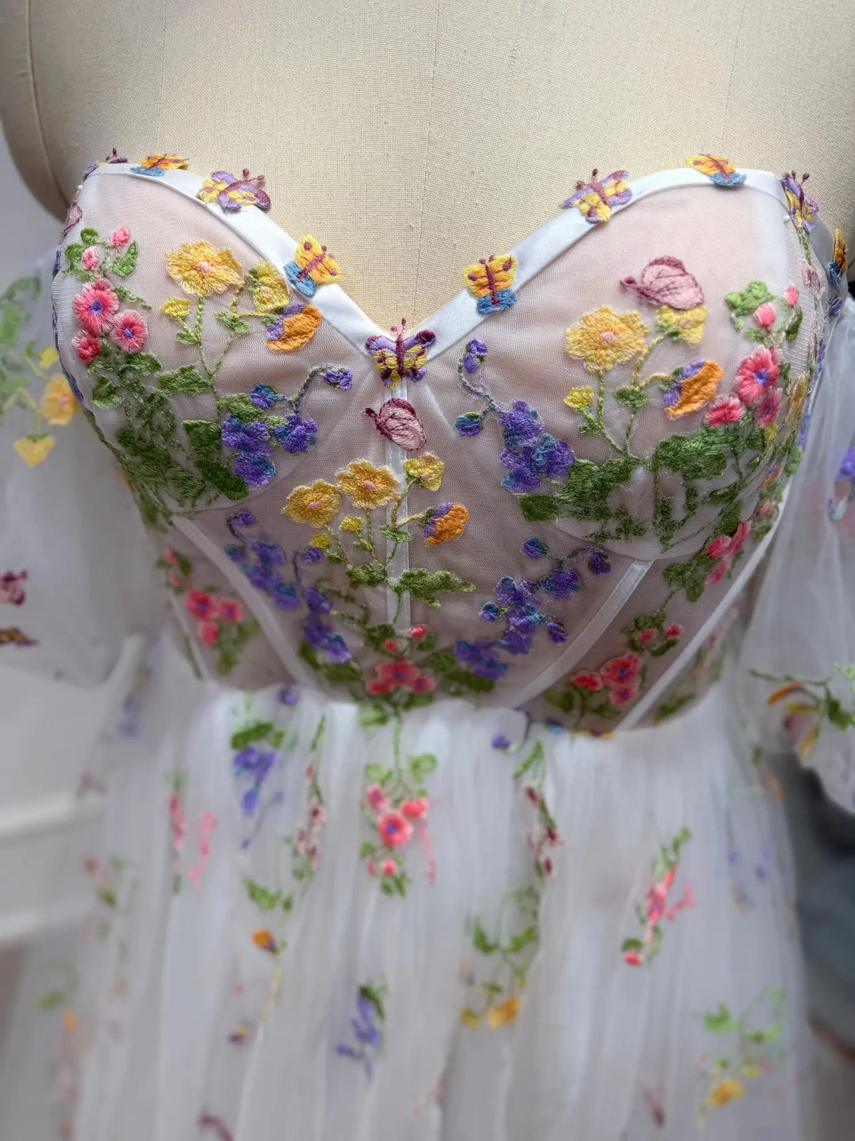 Corset bodice wedding dress with colorful floral embroidery and sheer tulle on a mannequin.