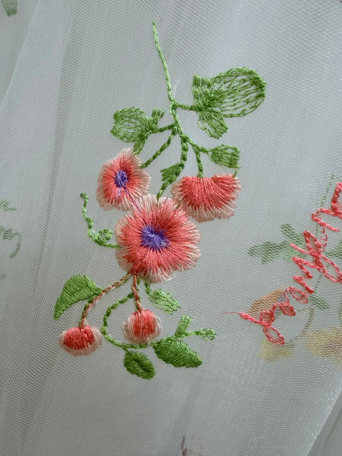 Close-up of delicate pastel floral embroidery with green leaves on airy white tulle fabric.