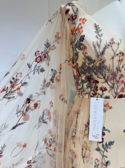 Elva botanical wedding dress in tulle with colorful wildflower embroidery and elegant flowing cape sleeves.