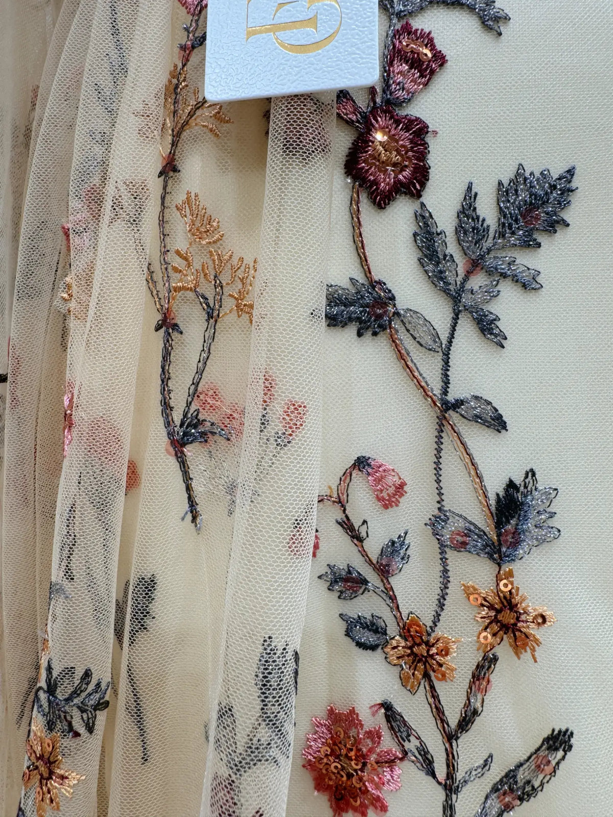 Sheer cream tulle wedding dress fabric featuring intricate wildflower meadow embroidery with metallic thread and sequins.
