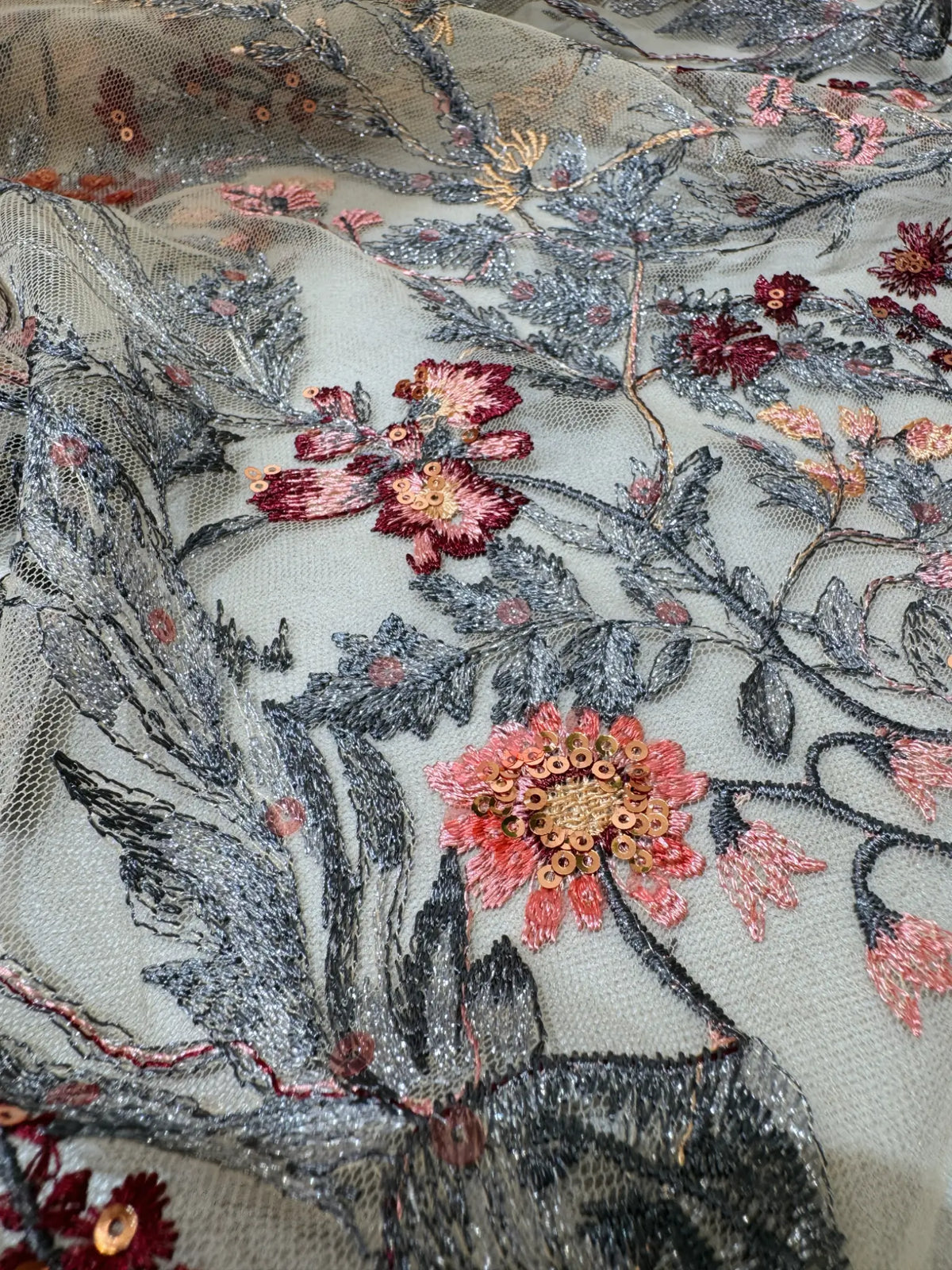 Sheer tulle fabric featuring intricate wildflower embroidery in metallic silver, pink, and deep red with sequin accents.