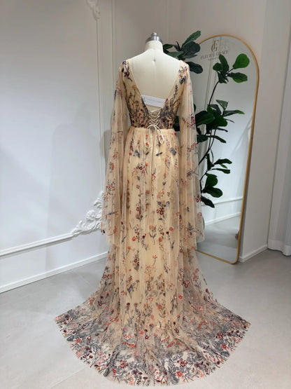 Backless botanical wedding dress with wildflower lace embroidery, cape sleeves, and a lace-up corset back on a mannequin.