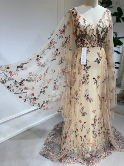 Elva botanical wedding dress with wildflower lace embroidery, V-neckline, and flowing cape sleeves on a mannequin.