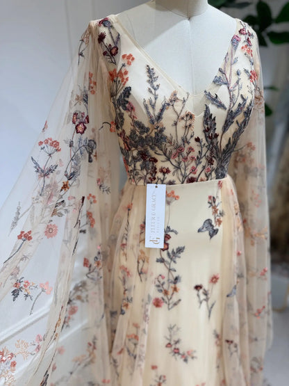 Elva wedding dress in sheer tulle with colorful wildflower embroidery, V-neckline, and elegant flowing cape sleeves.