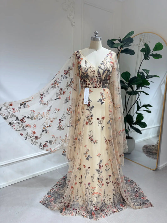Elva botanical wedding dress with wildflower lace embroidery, V-neckline, and flowing cape sleeves on a mannequin.