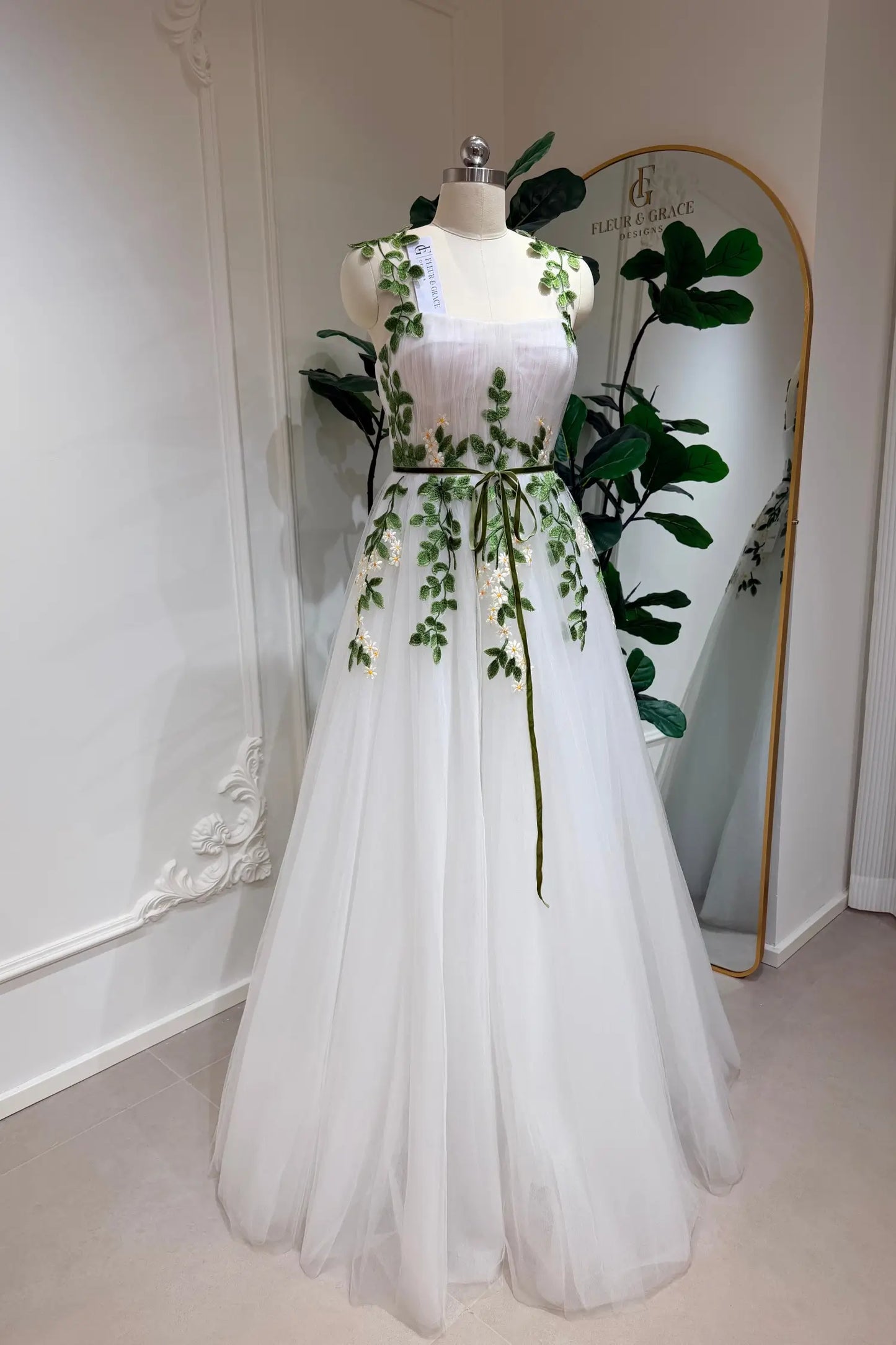 Ivory tulle A-line wedding gown featuring green leaf and daisy embroidery, a sweetheart bodice, and a thin green belt.