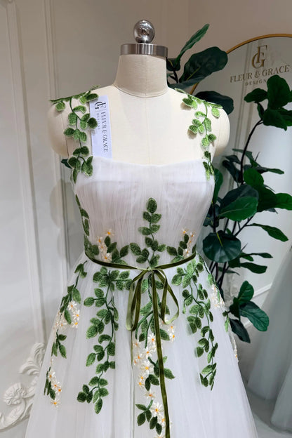 Ivory tulle wedding dress with green meadow embroidery, sweetheart bodice, and a thin green waist belt on a mannequin.