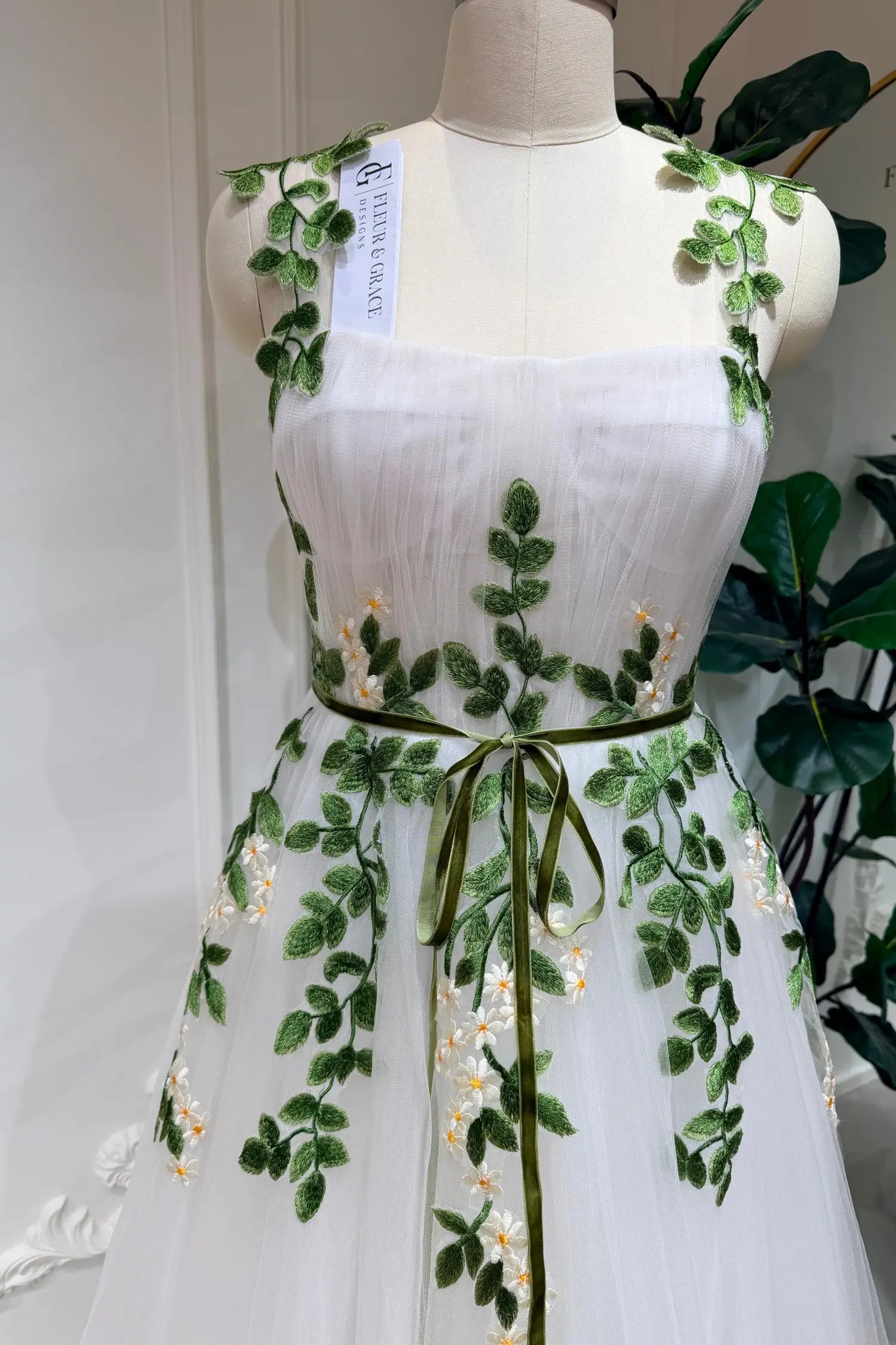 Ivory tulle wedding dress with green meadow daisy embroidery, sweetheart bodice, and a thin green waist ribbon.