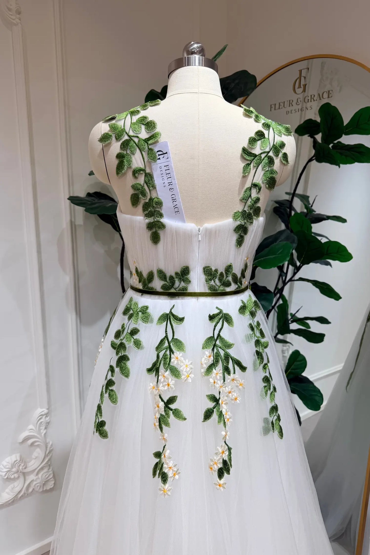 Ivory tulle wedding dress with green leaf and daisy embroidery, sweetheart bodice, and a thin green waist belt.