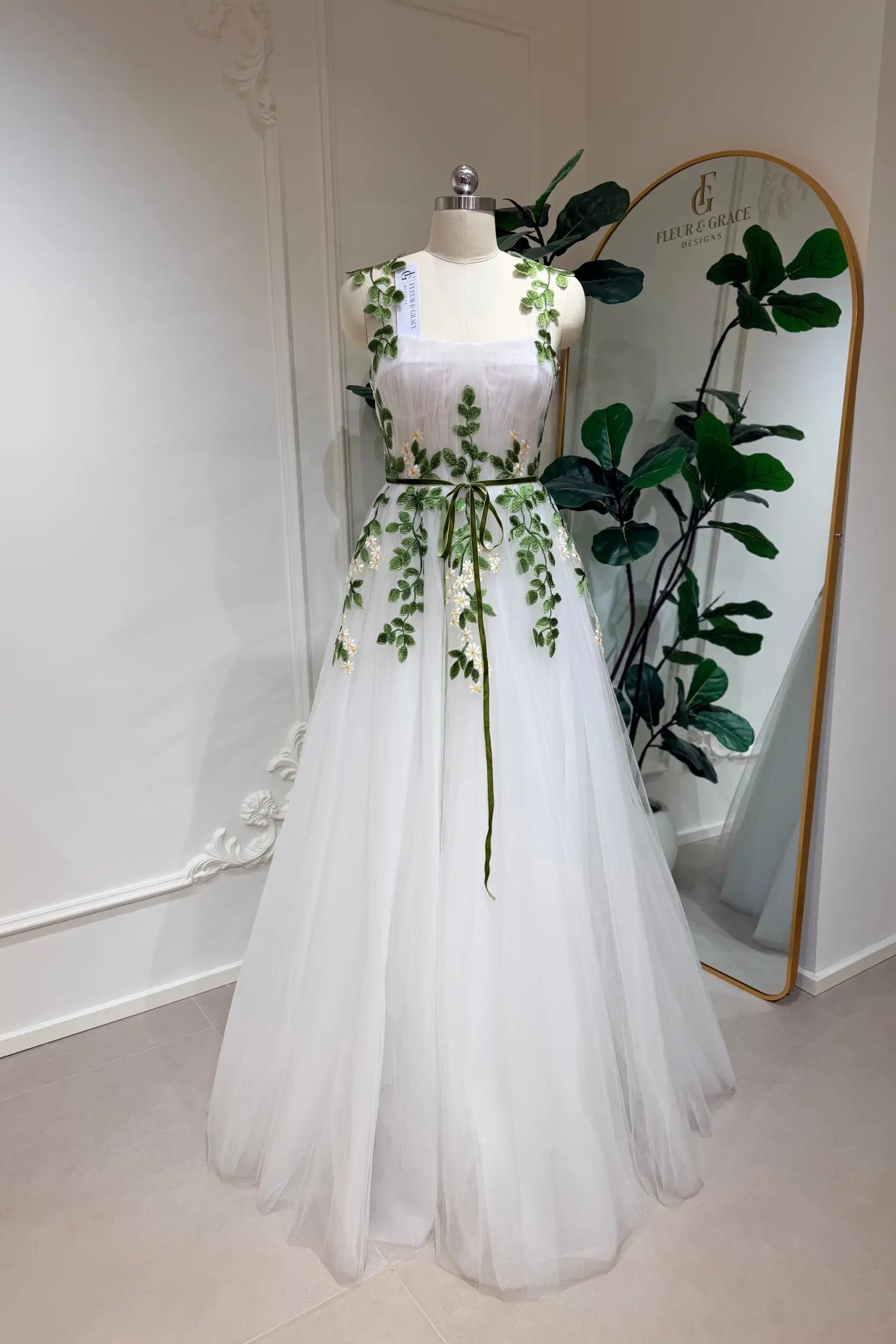 Ivory A-line tulle wedding gown with green meadow daisy embroidery, sweetheart bodice, and a thin green waist belt.